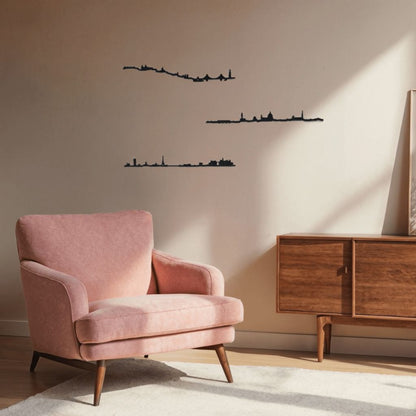 Espacio de lectura de estilo mid-century con butaca rosa empolvada sobre alfombra clara y aparador bajo de madera a la derecha; la pared beige, bañada por luz natural, luce tres siluetas negras de skylines decorativos: París (arriba), Lisboa (centro) y Florencia (abajo).