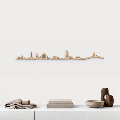 Skyline de Bielefeld en acabado marrón, presentado sobre el mueble blanco con lino, bobina de madera, libros y cerámica, en una decoración inspirada en la ciudad.