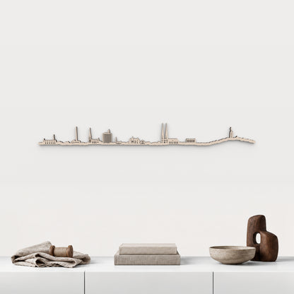 Skyline de Bielefeld en acabado natural, presentado sobre el mueble blanco con lino, bobina de madera, libros y cerámica, en una decoración inspirada en la ciudad.