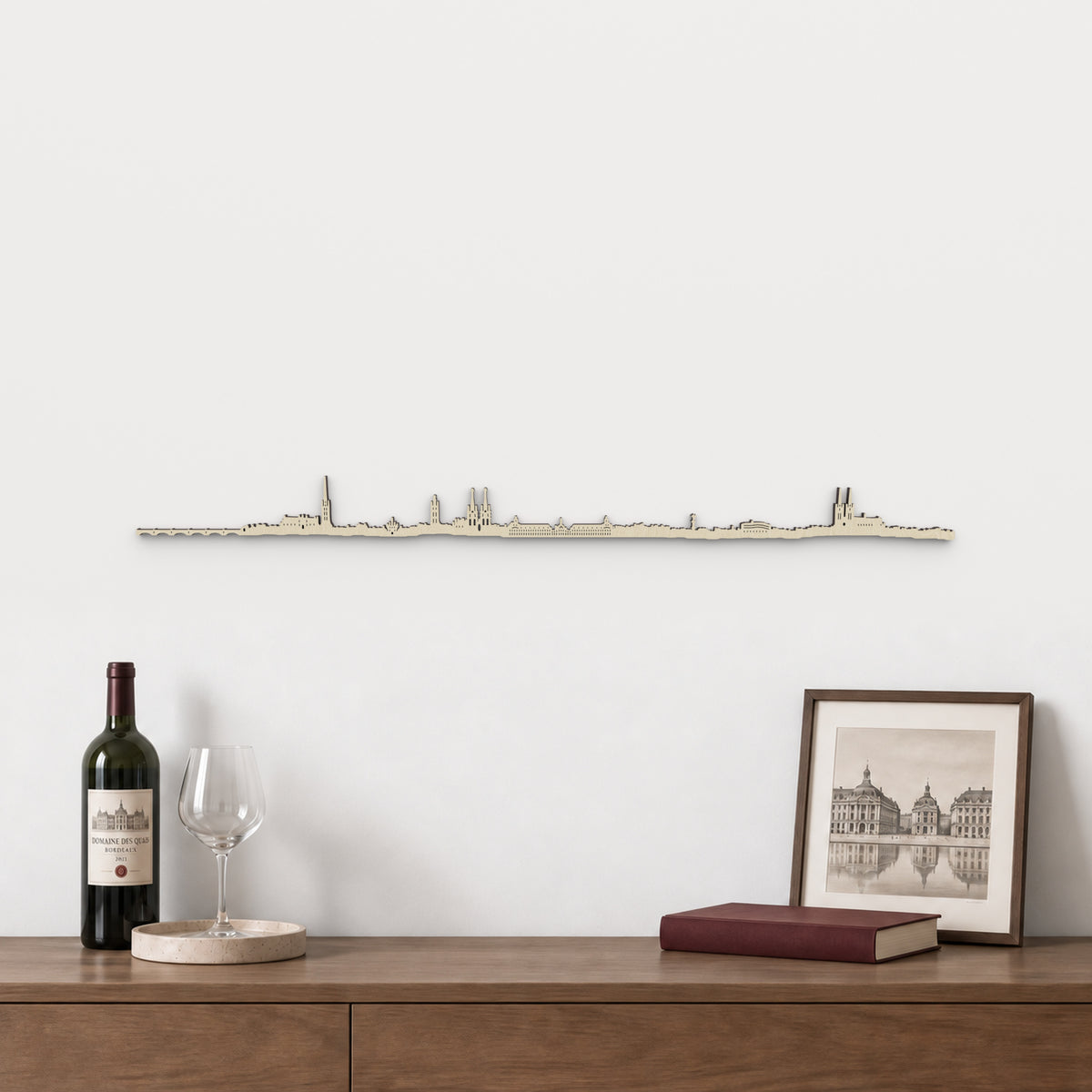 Skyline de Burdeos de 100 cm en madera natural, sobre aparador con vino, copa y lámina de arquitectura francesa.