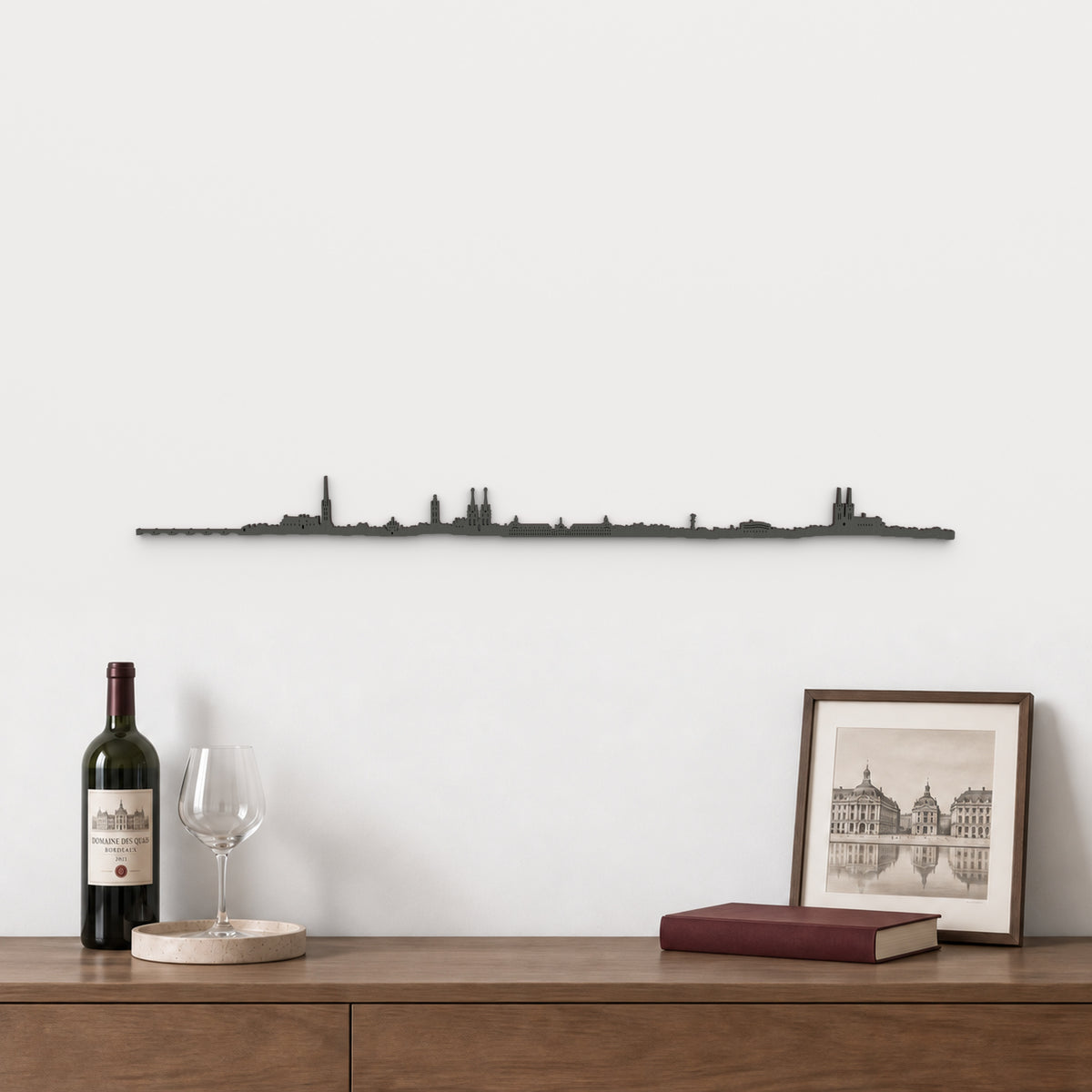 Skyline de Burdeos de 100 cm en madera con acabado negro, sobre aparador con vino, copa y lámina de arquitectura francesa.