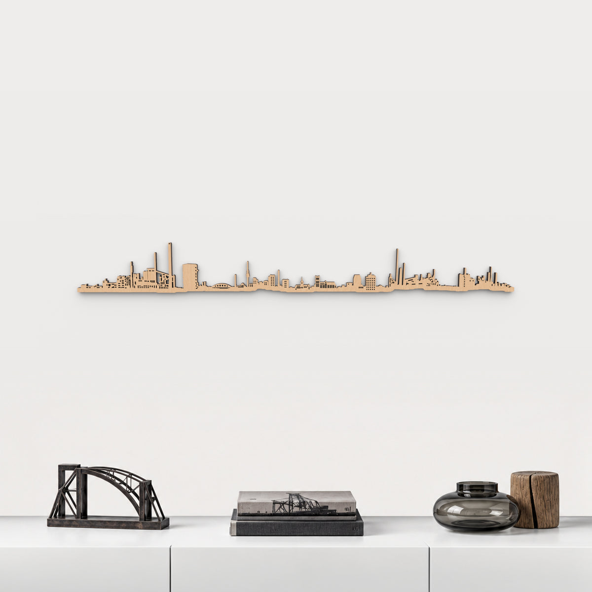 Skyline de Duisburg en acabado marrón, presentado sobre el mueble blanco con escultura de puente de acero, libros y vidrio ahumado, en una decoración inspirada en la ciudad.