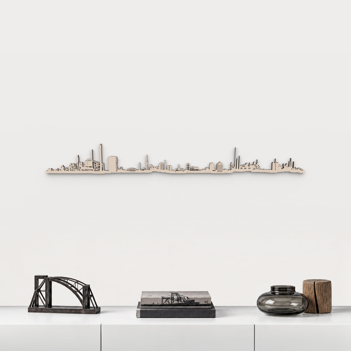 Skyline de Duisburg en acabado natural, presentado sobre el mueble blanco con escultura de puente de acero, libros y vidrio ahumado, en una decoración inspirada en la ciudad.