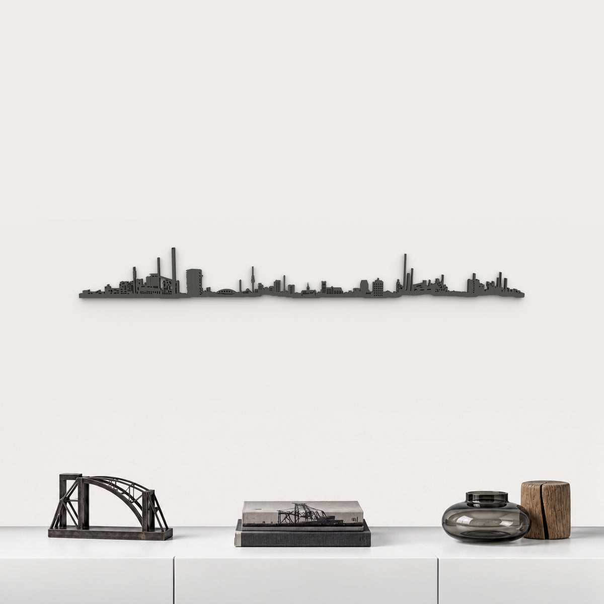 Skyline de Duisburg en acabado negro, presentado sobre el mueble blanco con escultura de puente de acero, libros y vidrio ahumado, en una decoración inspirada en la ciudad.