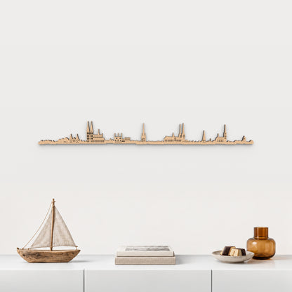 Skyline de Lübeck en acabado marrón, presentado sobre el mueble blanco con velero de madera, libros, mazapán y vidrio ámbar, en una decoración inspirada en la ciudad.