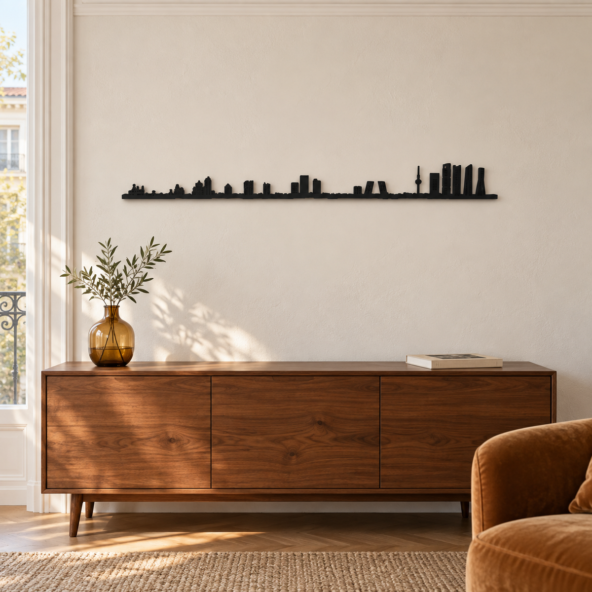 Skyline de Madrid en madera negra sobre un aparador con un jarrón ámbar, junto a una ventana.