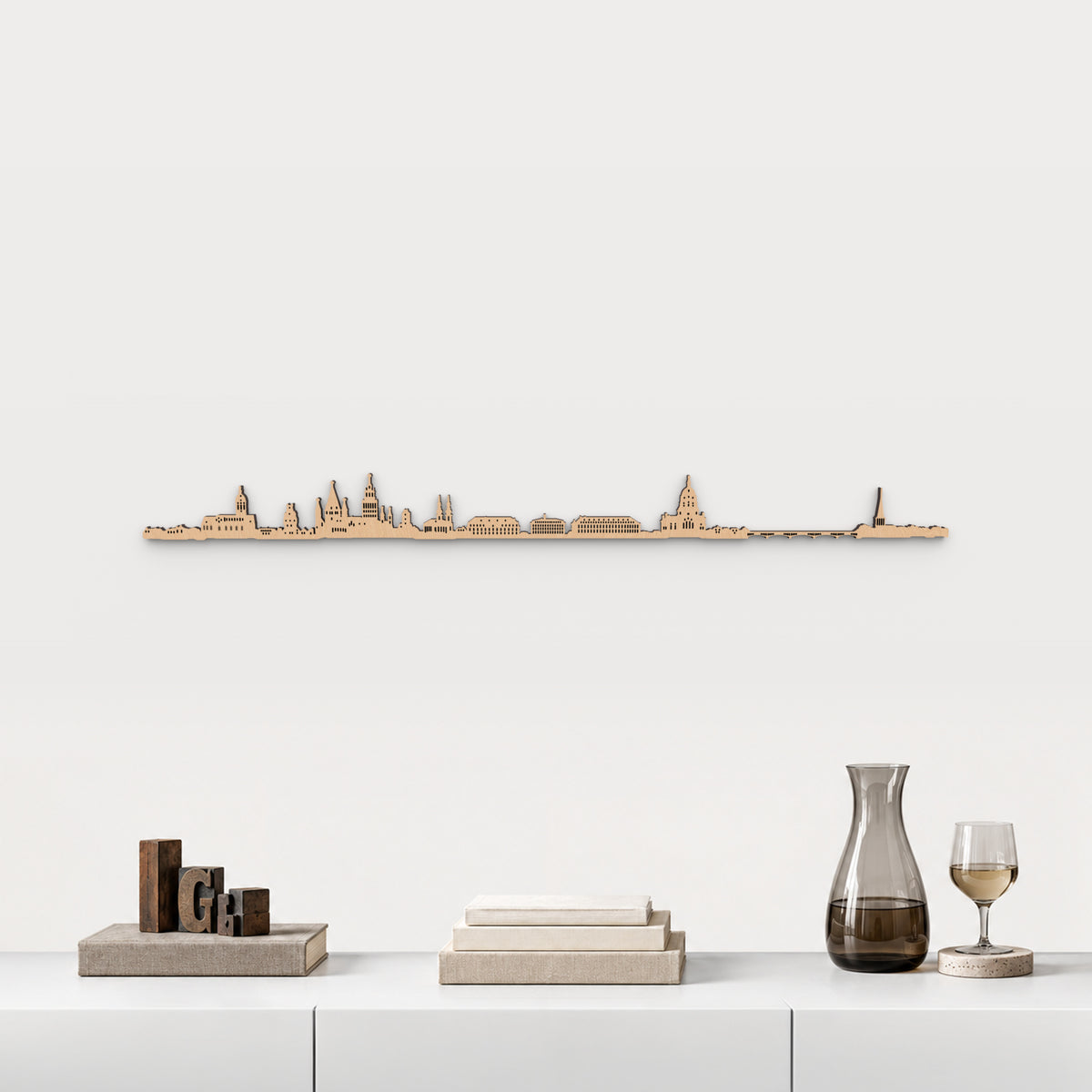 Skyline de Mainz en acabado marrón, presentado sobre el mueble blanco con tipos de imprenta, libros, decantador y copa de vino, en una decoración inspirada en la ciudad.