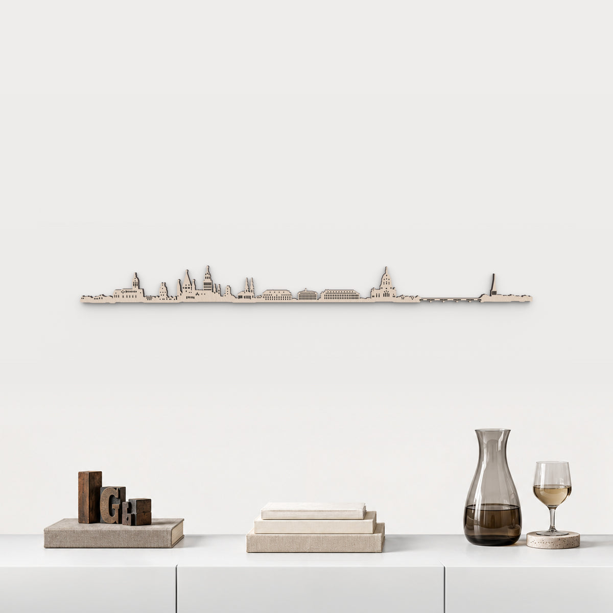 Skyline de Mainz en acabado natural, presentado sobre el mueble blanco con tipos de imprenta, libros, decantador y copa de vino, en una decoración inspirada en la ciudad.