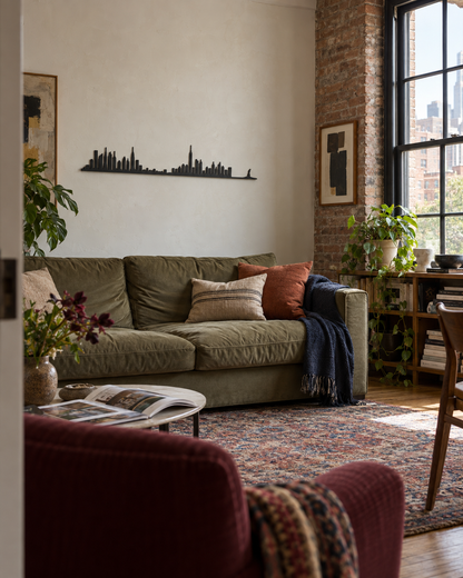 Skyline de Nueva York en madera negra sobre un sofá verde en un salón de estilo industrial.