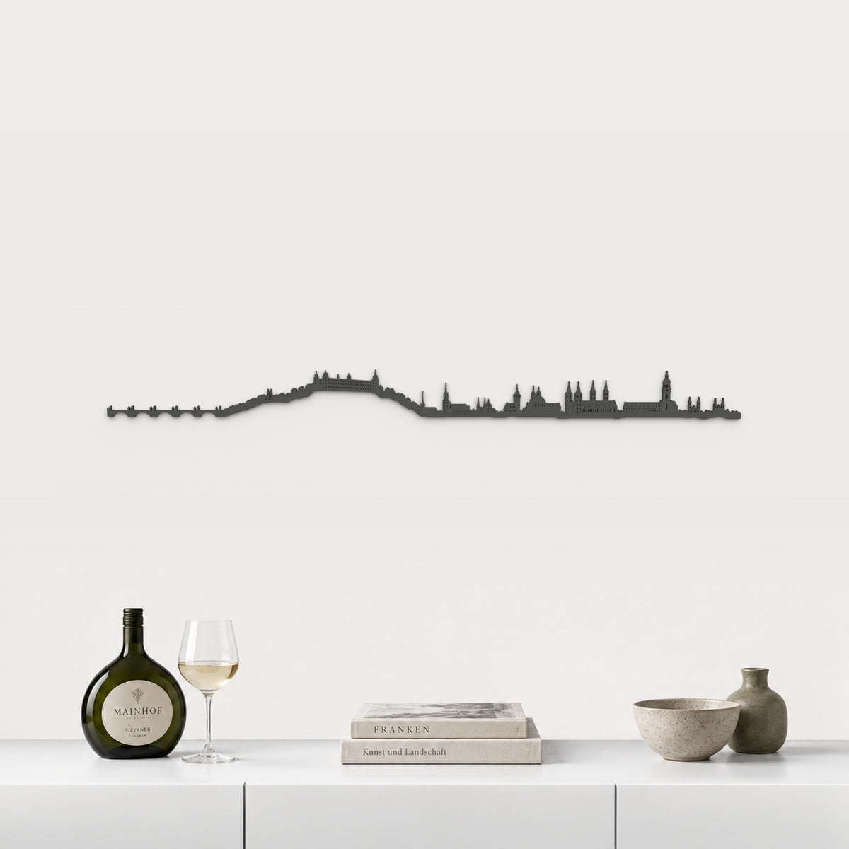 Skyline von Würzburg mit schwarzem Finish, 100 cm, über dem weißen Möbelstück mit fränkischem Wein, Büchern und Keramik, in einer von der Stadt inspirierten Einrichtung.